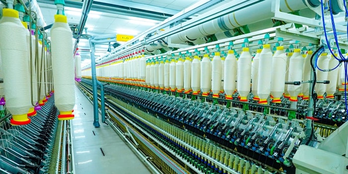 Textile spinning mill showing long rows of spindles with white yarn bobbins on an automated ring spinning machine