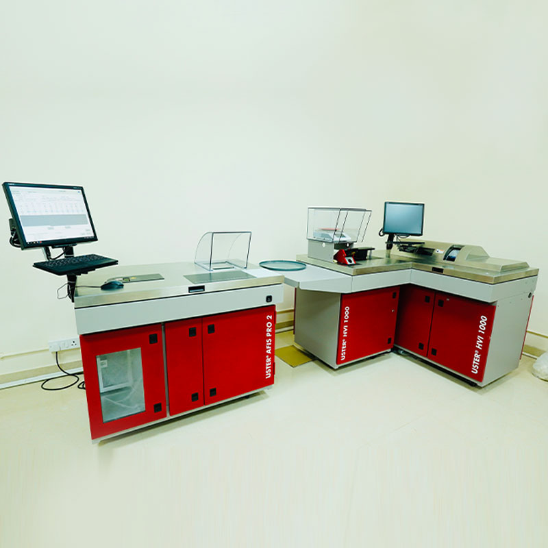 High-tech textile testing laboratory of NM Exports featuring red and grey Uster AFIS PRO 2 and HVI 1000 fiber testing instruments with computer monitors.