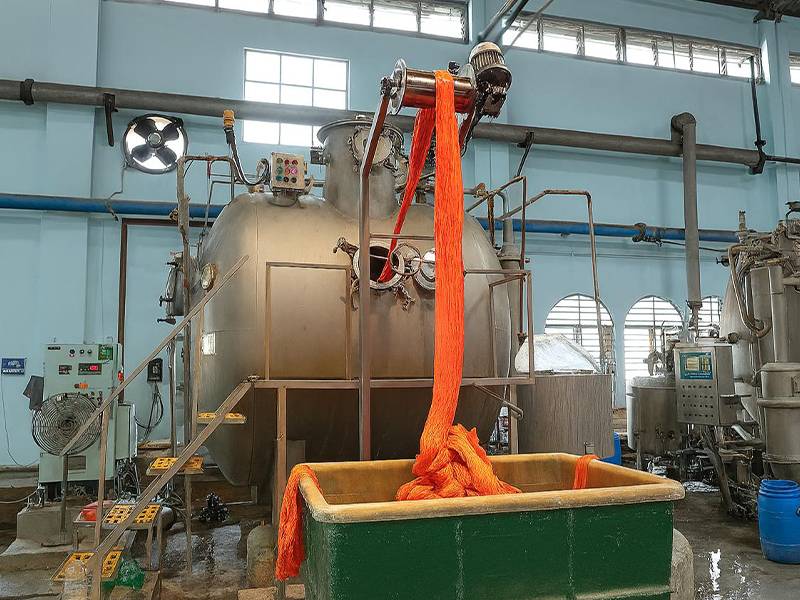 Bright orange yarn being pulled from a large, industrial silver dyeing machine into a green bin