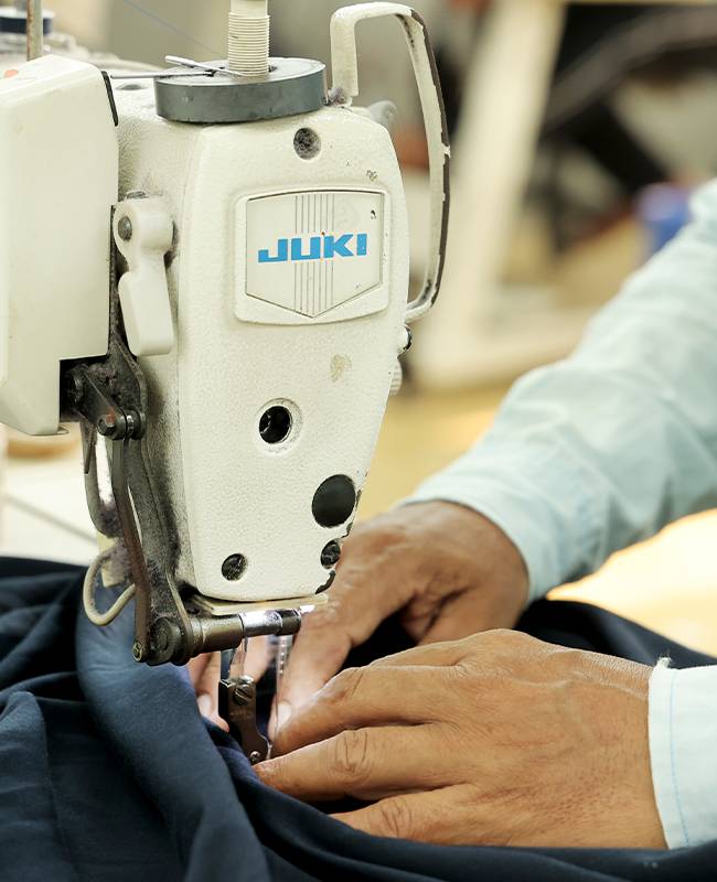 A worker's hands precisely guiding dark fabric through an industrial Juki sewing machine.
