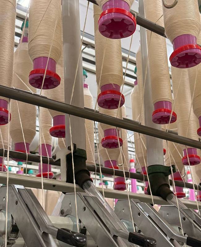 Multiple spools of off-white yarn with pink and red bases mounted on a spinning frame