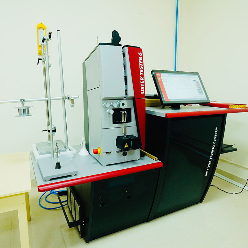 An Uster Tester 6 machine for evenness testing in textile laboratory of NM Exports, featuring a red and grey interface and a connected computer monitor